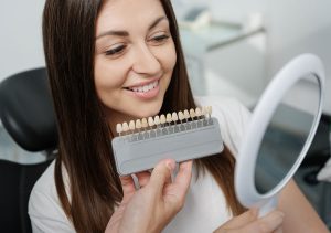 Image of a woman looking in a mirror to match her dental veneers to her teeth.