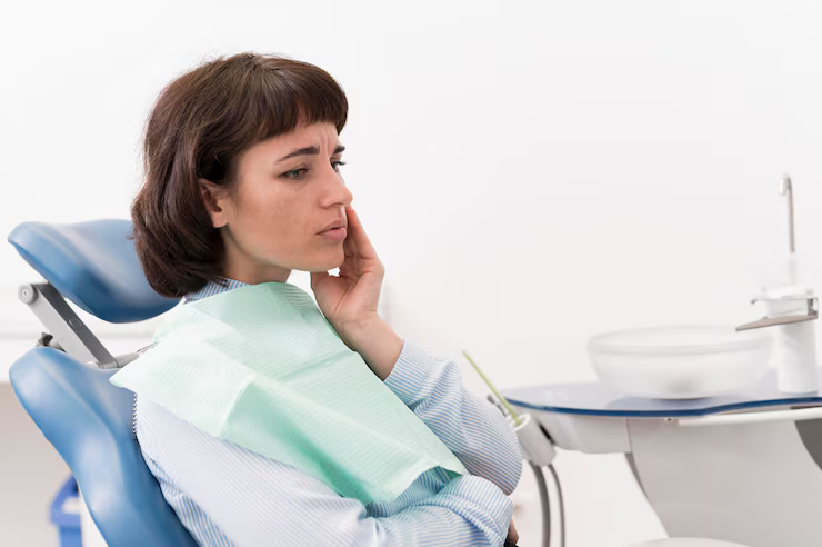 Woman in dentist chair holds face in discomfort.